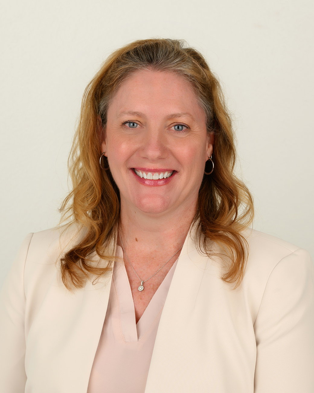 Christy Conrad smiling with blond hair and pink suit jacket